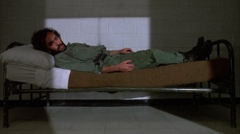 Movie still from “Day of the Dead” (1985), directed by George A. Romero – A man laying on a bed in a jail cell; Wide shot, High angle