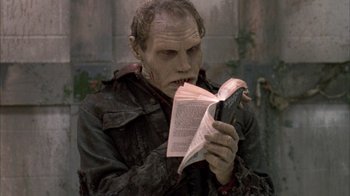Movie still from “Day of the Dead” (1985), directed by George A. Romero – A man with a zombie face reading a book; Close Up shot, High angle