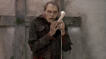 Movie still from “Day of the Dead” (1985), directed by George A. Romero – A man with a zombie makeup holding a phone; Medium shot, Low angle