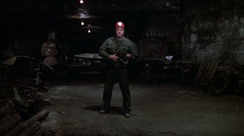 Movie still from “Day of the Dead” (1985), directed by George A. Romero – A man holding a rifle in a dark room; Wide shot, Low angle