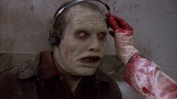 Movie still from “Day of the Dead” (1985), directed by George A. Romero – A person with a zombie mask and headphones on; Close Up shot, Over the shoulder angle