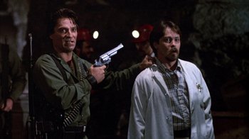 Movie still from “Day of the Dead” (1985), directed by George A. Romero – A man holding a gun pointed at another man in a lab coat; Medium shot, Over the shoulder angle