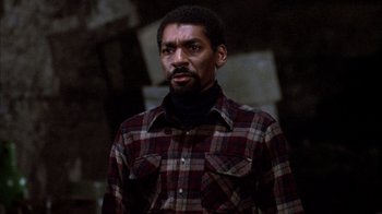 Movie still from “Day of the Dead” (1985), directed by George A. Romero – A man wearing a plaid shirt standing in a dark room; Close Up shot, Low angle