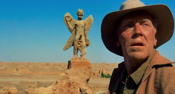 Movie still from “The Exorcist” (1973), directed by William Friedkin – A man standing next to a statue of an angel; Close Up shot, Low angle