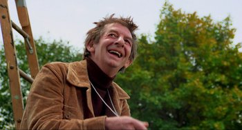 Movie still from “The Exorcist” (1973), directed by William Friedkin – An older man with spiky hair and a brown jacket; Medium shot, Low angle