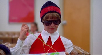 Movie still from “The Exorcist” (1973), directed by William Friedkin – A woman in a red and white outfit holding a gold chain; Close Up shot, Low angle