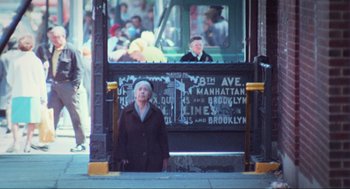 Movie still from “The Exorcist” (1973), directed by William Friedkin – An older woman standing in front of a bus stop; Wide shot, High angle