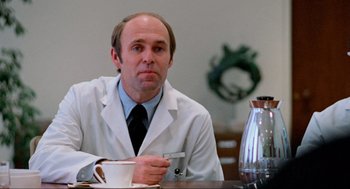 Movie still from “The Exorcist” (1973), directed by William Friedkin – A man sitting at a table with a cup of coffee; Medium shot, Low angle