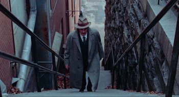 Movie still from “The Exorcist” (1973), directed by William Friedkin – An older man in a hat and coat walking down the stairs; Wide shot, High angle