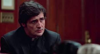 Movie still from “The Exorcist” (1973), directed by William Friedkin – A man wearing a priest's outfit looking to his left; Close Up shot, Over the shoulder angle