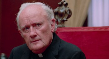 Movie still from “The Exorcist” (1973), directed by William Friedkin – An older man in a priest's outfit sitting in a chair; Close Up shot, Over the shoulder angle