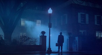 Movie still from “The Exorcist” (1973), directed by William Friedkin – A man standing next to a street light on a foggy night; Wide shot, Low angle