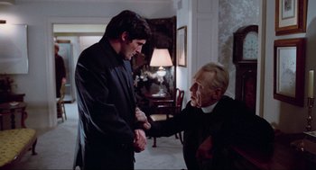 Movie still from “The Exorcist” (1973), directed by William Friedkin – A man and a priest shaking hands in a living room; Medium shot, Over the shoulder angle