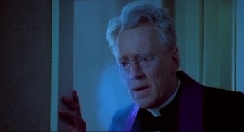 Movie still from “The Exorcist” (1973), directed by William Friedkin – An older man wearing glasses and a priest's outfit; Close Up shot, Low angle