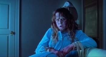 Movie still from “The Exorcist” (1973), directed by William Friedkin – A young girl dressed as the exorcist sitting in a chair; Medium shot, High angle