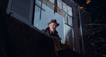 Movie still from “The Exorcist” (1973), directed by William Friedkin – A man wearing a hat looking out of a window; Wide shot, Low angle