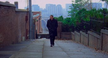 Movie still from “The Exorcist” (1973), directed by William Friedkin – A man walking down the street holding a skateboard; Wide shot, Low angle