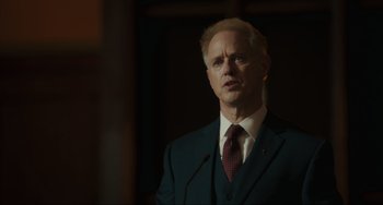 Movie still from “The Exorcist: Believer” (2023), directed by David Gordon Green – A man wearing a suit and tie standing in front of a microphone; Close Up shot, Low angle