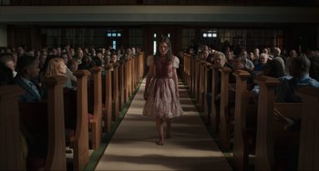 Movie still from “The Exorcist: Believer” (2023), directed by David Gordon Green – A woman in a dress walking down a long aisle of wooden pews; Wide shot, High angle