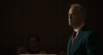 Movie still from “The Exorcist: Believer” (2023), directed by David Gordon Green – A man standing at a podium in front of a microphone; Close Up shot, Low angle