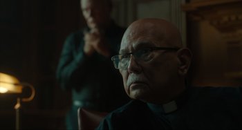 Movie still from “The Exorcist: Believer” (2023), directed by David Gordon Green – An older man wearing glasses and wearing a priest's collar; Close Up shot, Over the shoulder angle