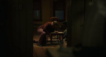 Movie still from “The Exorcist: Believer” (2023), directed by David Gordon Green – A man sitting on top of a chair in a living room; Wide shot, High angle