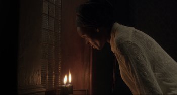 Movie still from “The Exorcist: Believer” (2023), directed by David Gordon Green – A woman standing in front of a lit candle in a dark room; Medium shot, Low angle
