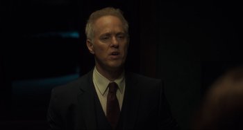 Movie still from “The Exorcist: Believer” (2023), directed by David Gordon Green – A man in a suit and tie standing in a dark room; Close Up shot, Over the shoulder angle