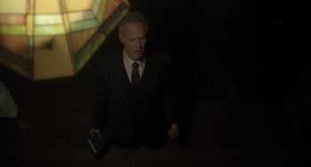 Movie still from “The Exorcist: Believer” (2023), directed by David Gordon Green – A man in a suit kneeling on the ground holding a book; Medium shot, High angle