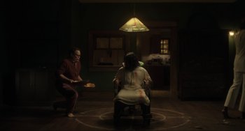 Movie still from “The Exorcist: Believer” (2023), directed by David Gordon Green – A man and a woman sitting on a chair in a room; Wide shot, High angle