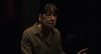 Movie still from “The Exorcist: Believer” (2023), directed by David Gordon Green – A man in a green shirt is sitting in a dark room; Close Up shot, Over the shoulder angle