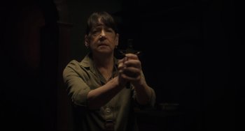 Movie still from “The Exorcist: Believer” (2023), directed by David Gordon Green – A woman holding a gun in a dark room; Medium shot, Over the shoulder angle