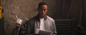 Movie still from “The Fate of the Furious” (2017), directed by F. Gary Gray – A man is holding papers while sitting in a chair; Close Up shot, Over the shoulder angle