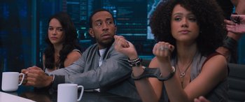 Movie still from “The Fate of the Furious” (2017), directed by F. Gary Gray – A group of people sitting at a table with a cup of coffee; Medium shot, Over the shoulder angle