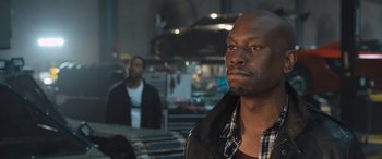 Movie still from “The Fate of the Furious” (2017), directed by F. Gary Gray – A man standing next to another man in front of a building; Close Up shot, Over the shoulder angle