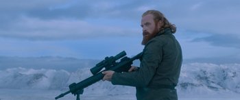 Movie still from “The Fate of the Furious” (2017), directed by F. Gary Gray – A man with a long beard holding a rifle; Medium shot, Over the shoulder angle
