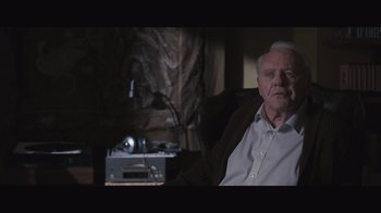 Movie still from “The Father” (2020), directed by Florian Zeller – An older man sitting in a chair in front of a television; Medium shot, Over the shoulder angle