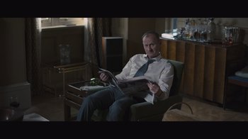 Movie still from “The Father” (2020), directed by Florian Zeller – A man sitting in a chair holding a newspaper; Medium shot, High angle