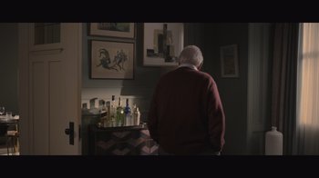 Movie still from “The Father” (2020), directed by Florian Zeller – An older man standing in front of a table with bottles of alcohol; Medium shot, Over the shoulder angle