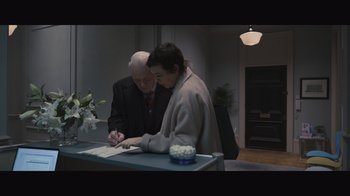Movie still from “The Father” (2020), directed by Florian Zeller – A man and a woman signing a document; Medium shot, High angle