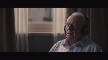Movie still from “The Father” (2020), directed by Florian Zeller – An older man wearing headphones while sitting in front of a window; Close Up shot, High angle
