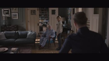 Movie still from “The Father” (2020), directed by Florian Zeller – A man sitting in a chair in front of two women; Wide shot, Over the shoulder angle