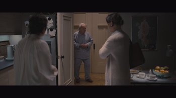Movie still from “The Father” (2020), directed by Florian Zeller – An old man standing in a room with two young women; Wide shot, High angle