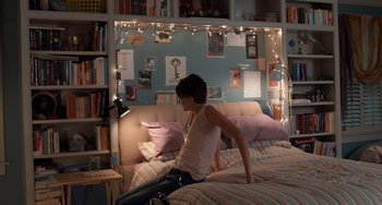 Movie still from “The Fault in Our Stars” (2014), directed by Josh Boone – A person sitting on top of a bed in a room; Wide shot, High angle
