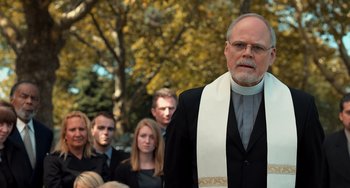 Movie still from “The Fault in Our Stars” (2014), directed by Josh Boone – A man in a priest's outfit standing in front of a group of people; Medium shot, Over the shoulder angle