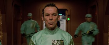 Movie still from “The Fifth Element” (1997), directed by Luc Besson – A man in a green shirt is standing in front of a mirror; Close Up shot, Low angle