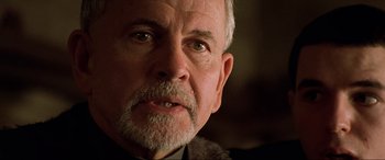 Movie still from “The Fifth Element” (1997), directed by Luc Besson – An older man with a gray beard looking at the camera; Close Up shot, Over the shoulder angle