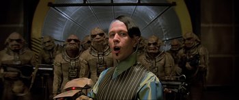 Movie still from “The Fifth Element” (1997), directed by Luc Besson – A man in a striped vest standing in front of a group of other men; Medium shot, Over the shoulder angle