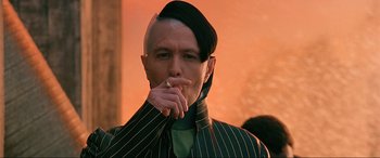 Movie still from “The Fifth Element” (1997), directed by Luc Besson – A man with a shaved head smoking a cigarette in front of an orange background; Close Up shot, Low angle