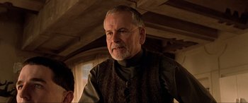 Movie still from “The Fifth Element” (1997), directed by Luc Besson – An older man wearing a brown vest looking at the camera; Close Up shot, Over the shoulder angle